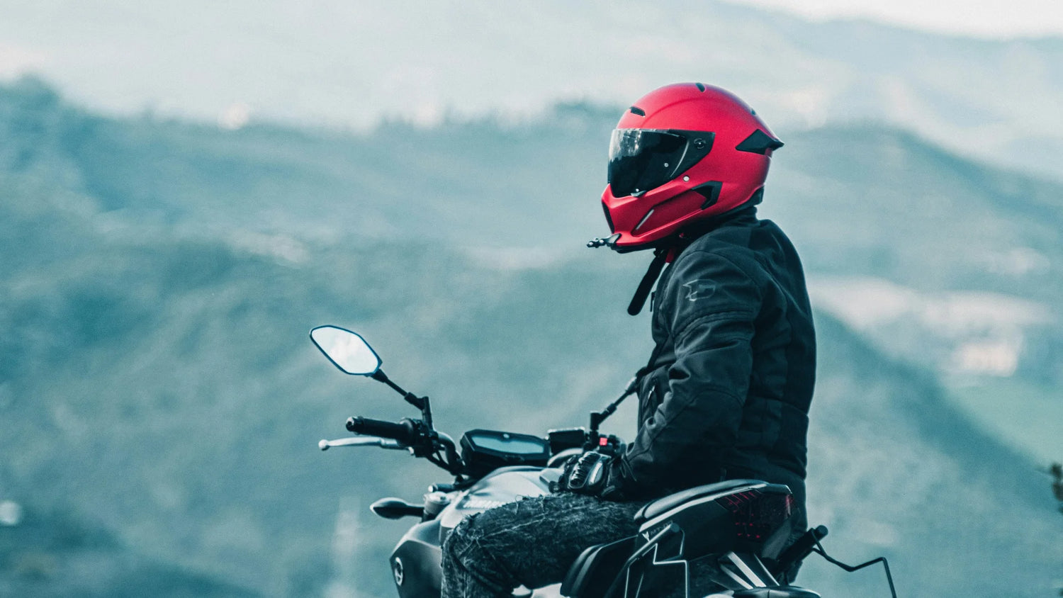 Motorrijder met rode motorhelm en motorkleding in berglandschap – geschikte motorkleding voor elk seizoen